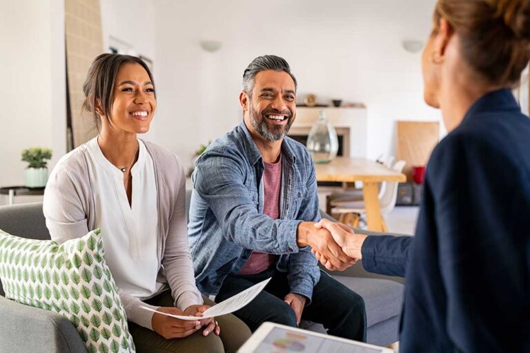 A real estate agent and home buyers discussing paperwork at a kitchen table in a bright residential home.
